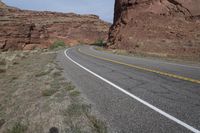 a person riding a motorcycle along a narrow road through rocks and sand cliffs a grassy area on both sides