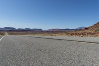 a lone car is driving on a desert highway with mountains in the background of the road