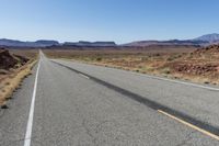 a lone car is driving on a desert highway with mountains in the background of the road