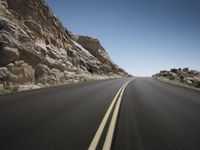 the empty road stretches beside a cliff in an arid area of some sort or on other side