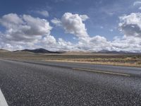 a wide open road that leads into the desert area, a cloud filled sky with some white clouds