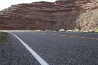 a person riding a motorcycle along a narrow road through rocks and sand cliffs a grassy area on both sides