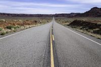 an empty paved road is surrounded by desert scenery and mountains as the sun shines on the horizon