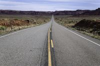 an empty paved road is surrounded by desert scenery and mountains as the sun shines on the horizon