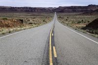 an empty paved road is surrounded by desert scenery and mountains as the sun shines on the horizon