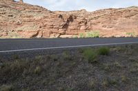 a person riding a motorcycle along a narrow road through rocks and sand cliffs a grassy area on both sides