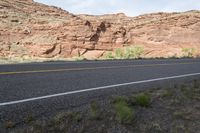 a person riding a motorcycle along a narrow road through rocks and sand cliffs a grassy area on both sides