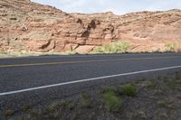 a person riding a motorcycle along a narrow road through rocks and sand cliffs a grassy area on both sides