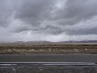 gray sky over the desert with mountains in the background and wet pavement along side a country road