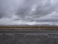 gray sky over the desert with mountains in the background and wet pavement along side a country road