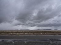 gray sky over the desert with mountains in the background and wet pavement along side a country road