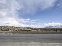 a motorcycle riding on the street beside a hill on a sunny day with cloudy sky