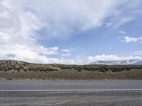 a motorcycle riding on the street beside a hill on a sunny day with cloudy sky