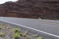 a person riding a motorcycle along a narrow road through rocks and sand cliffs a grassy area on both sides