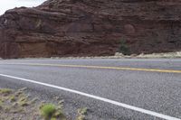 a person riding a motorcycle along a narrow road through rocks and sand cliffs a grassy area on both sides