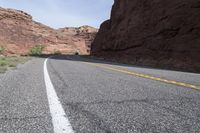 a person riding a motorcycle along a narrow road through rocks and sand cliffs a grassy area on both sides