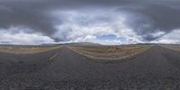 a long road with a yellow line at the ends and storm clouds above it in the distance