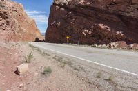 an empty road runs along a desert like terrain with a rock in the foreground