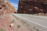 an empty road runs along a desert like terrain with a rock in the foreground