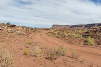 a dirt road is running through a rocky desert landscape with a sky background and some brown rocks