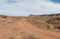 a dirt road is running through a rocky desert landscape with a sky background and some brown rocks