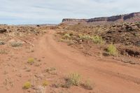 a dirt road is running through a rocky desert landscape with a sky background and some brown rocks