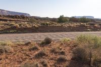 a desert and mountain scene with dirt, shrubs, and rocks in the foreground