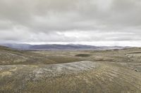 a lone person is walking through the barren hills on a cloudy day, and there are mountains in the distance