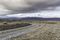 an empty road surrounded by barren mountains and bushes under a cloudy sky, as if in nature