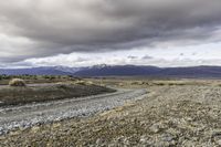 an empty road surrounded by barren mountains and bushes under a cloudy sky, as if in nature