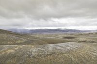 a person is sitting on a rock in the desert near mountains under a cloudy sky