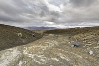 a barren area with rocks and dirt on the ground with mountains in the distance and clouds