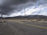 a railroad crossing sign near a highway with mountains in the background in front of clouds