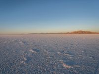 an empty, flat desert at sunrise with mountains in the distance and no clouds in sight