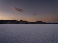 a man in blue snow skis on a vast expanse of salt and sky at dusk