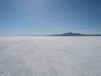 the sky is blue and clear as it sits over a white salt flat field with a single vehicle in the distance