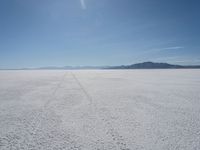 the sky is blue and clear as it sits over a white salt flat field with a single vehicle in the distance