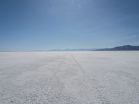 the sky is blue and clear as it sits over a white salt flat field with a single vehicle in the distance