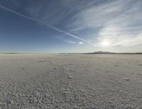 an expanse of white salt with blue sky above and a lone jet trail in the background