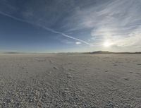 an expanse of white salt with blue sky above and a lone jet trail in the background