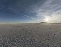 an expanse of white salt with blue sky above and a lone jet trail in the background