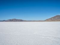 a large open plain with sparse snow capped mountains in the distance, with a man on a motorbike crossing