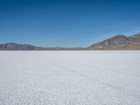 a large open plain with sparse snow capped mountains in the distance, with a man on a motorbike crossing