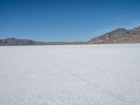 a large open plain with sparse snow capped mountains in the distance, with a man on a motorbike crossing