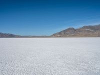 a large open plain with sparse snow capped mountains in the distance, with a man on a motorbike crossing