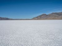 a large open plain with sparse snow capped mountains in the distance, with a man on a motorbike crossing