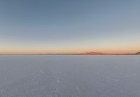 an image of the sun setting over a mountain range on the salt flat field in the foreground