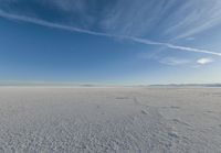 the vast expanse is covered in snow and clouds under a blue sky, with a lone person walking on one side