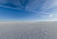 the vast expanse is covered in snow and clouds under a blue sky, with a lone person walking on one side