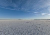 the vast expanse is covered in snow and clouds under a blue sky, with a lone person walking on one side